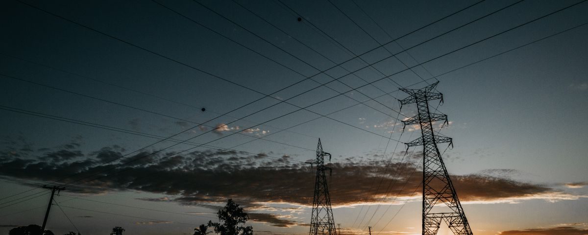 Lattice transmission towers and power lines silhouetted at sunset